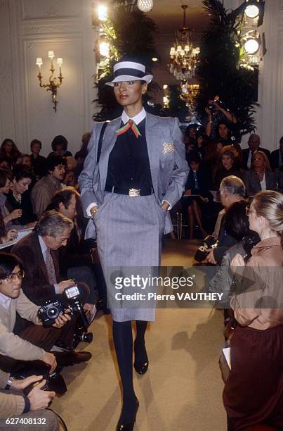 Fashion model wears a gray haute couture blazer and straight skirt with a brimmed hat by French fashion designer Marc Bohan for French fashion house...