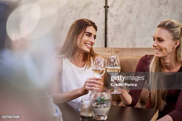 lächelnde frauen rösten weingläser im restaurant - freundinnen wein stock-fotos und bilder