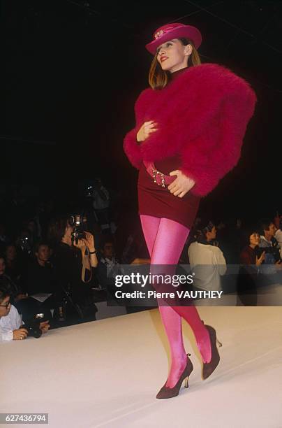 Fashion model wears a fuzzy, red haute couture jacket and short skirt with hot pink stockings and a brimmed hat by French fashion designer Chantal...