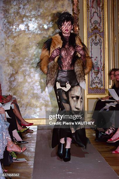 Fashion model wearing a women's haute couture black skirt with a face on it, brown fur jacket, and a sheer black lace top and hat designed by French...