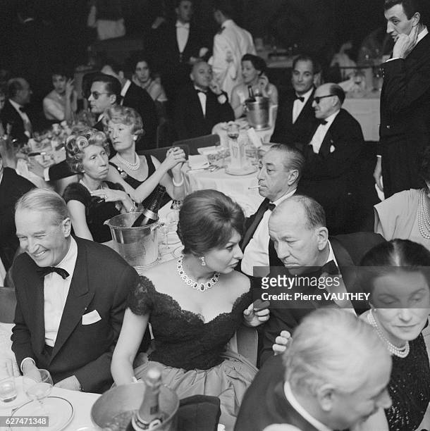 Sophia Loren, seated next to Maurice Chevalier, speaks with Noel Coward during a dinner event in Paris.