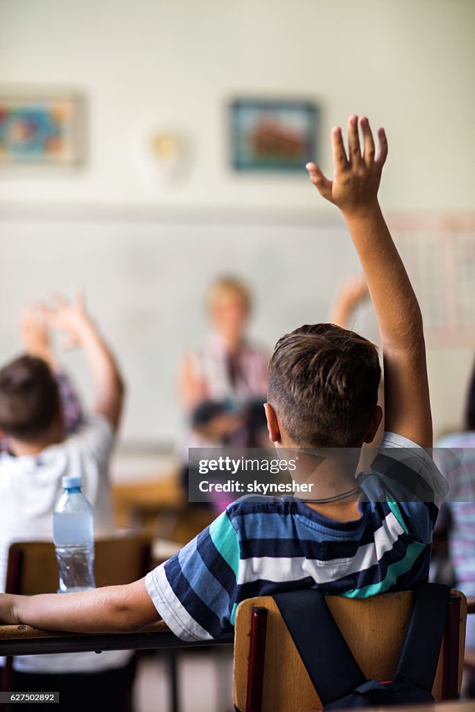 Rückansicht des Schülers mit erhobener Hand im Klassenzimmer.