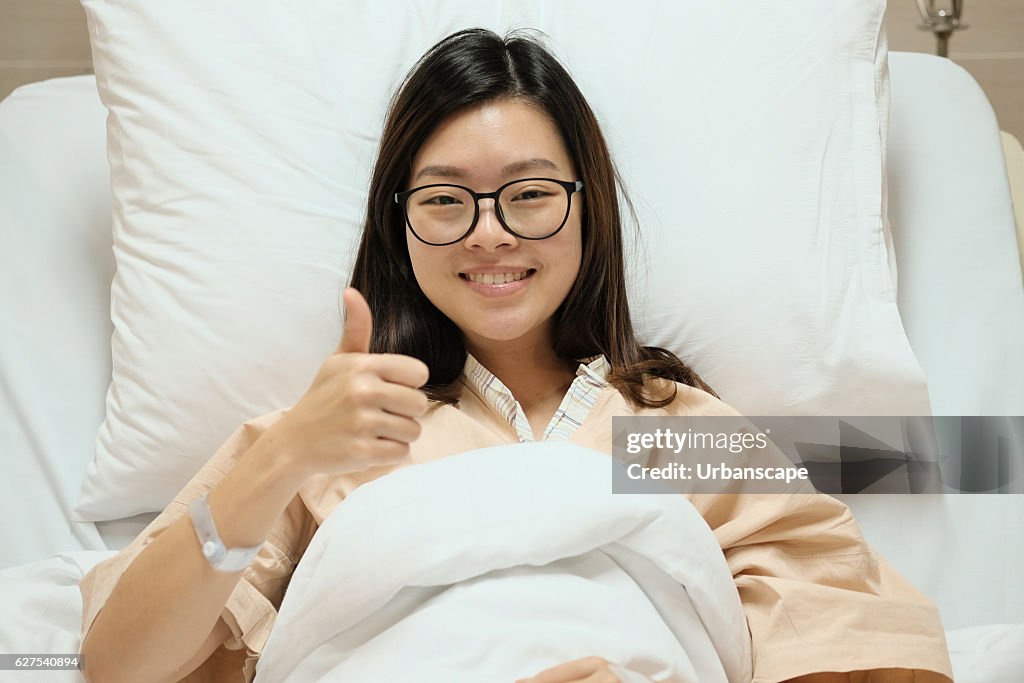 Asian patient girl thumbs up and smile on hospital bed