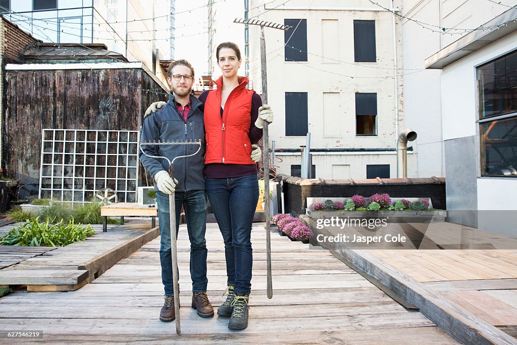 Couple holding rakes in urban rooftop garden