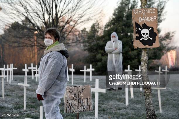 People wearing masks and protective suits stand next placards which translates as "Gironde in danger", "trade secret" and white crosses planted by...