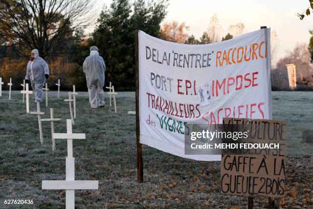 People wearing masks and protective suits stand next to banner which translates as "period of "entry" shortened, E.P.I imposed, wine workers...