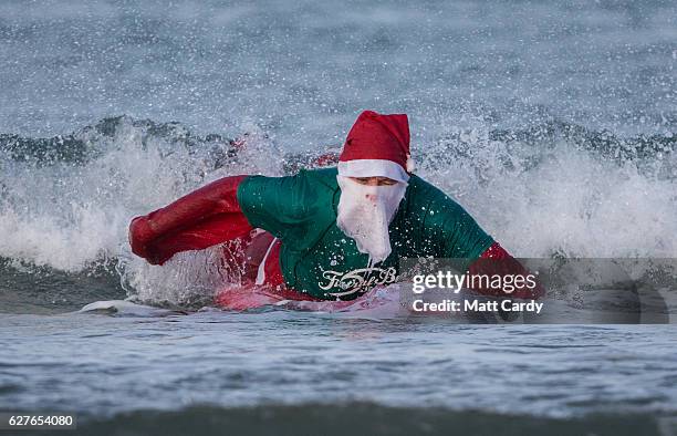 Surfer dressed as Santa tries to get to his feet as he braves the cold seas and near flat waves during the annual Surfing Santa as part of the Santa...