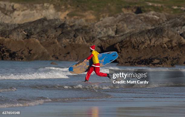 Surfer dressed as Santa runs to sea as he competes in a heat during the annual Surfing Santa as part of the Santa Run and Surf 2016 at Fistral Beach...