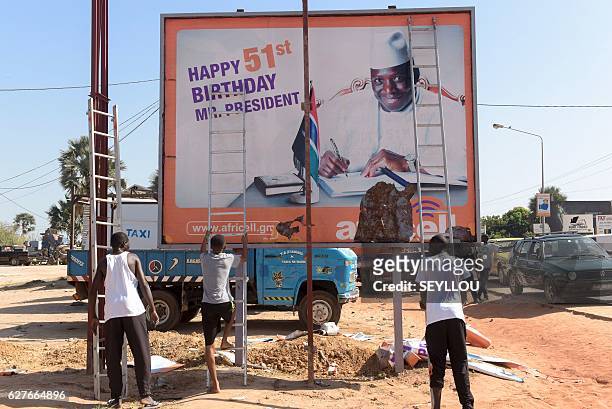 Workers prepare to remove an electoral poster of Gambia's outgoing president Yahya Jammeh, in a street of Bijilo, on December 4, 2016. Opposition...