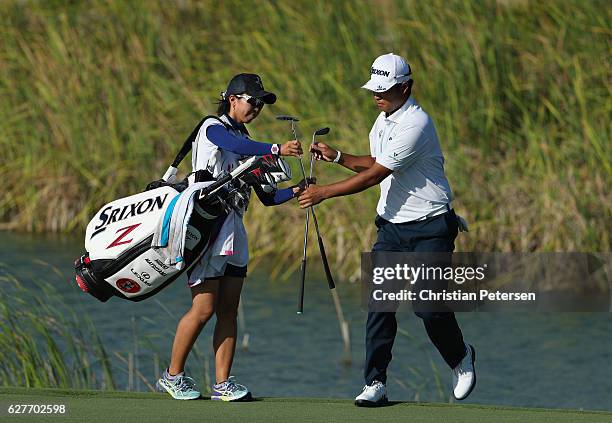 Hideki Matsuyama of Japan swaps clubs with caddie Mei Inui after chipping to the 12th green during the final round of the Hero World Challenge at...