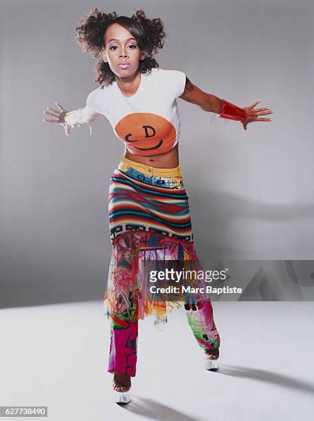 Lisa "Left Eye" Lopes of the popular R&B group TLC. She wears a short-sleeved Christian Dior t-shirt with a multi-colored miniskirt over pants.