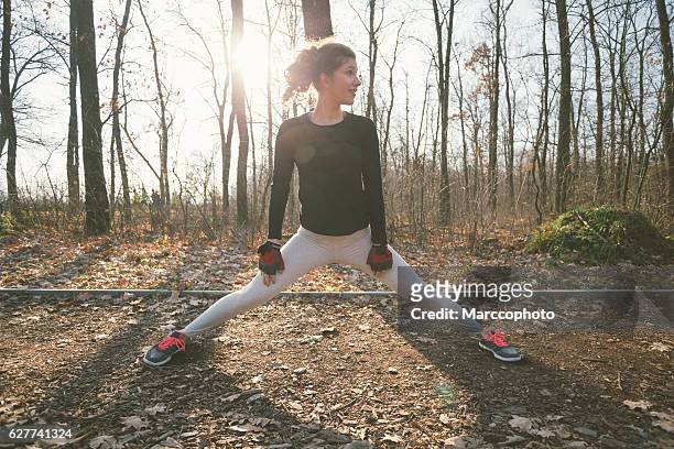 attractive young girl exercising outdoors, stretching legs on the ground - leg stretch girl stock pictures, royalty-free photos & images