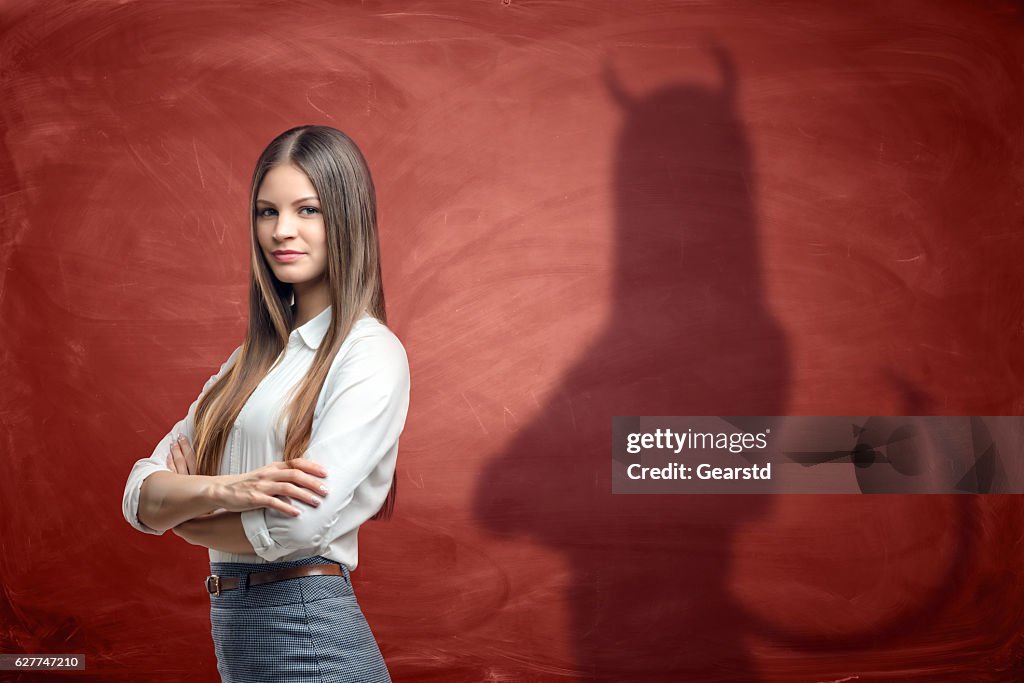 Young businesswoman is casting shadow of devil on rusty orange