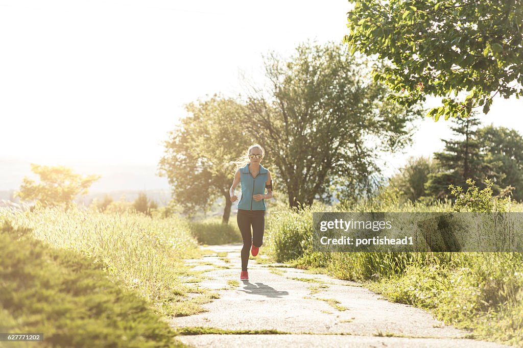 Front view of woman running on sunny trail in park