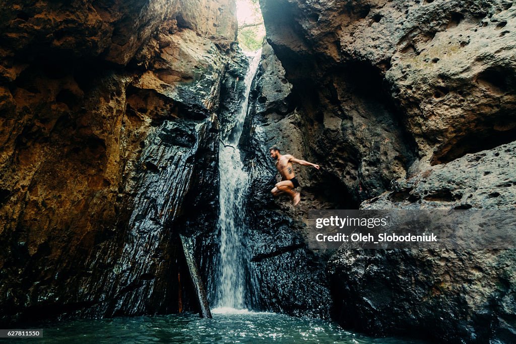 Man jumping into tropical waterfall