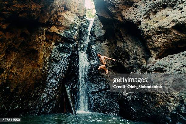 man jumping into tropical waterfall - waterval stockfoto's en -beelden