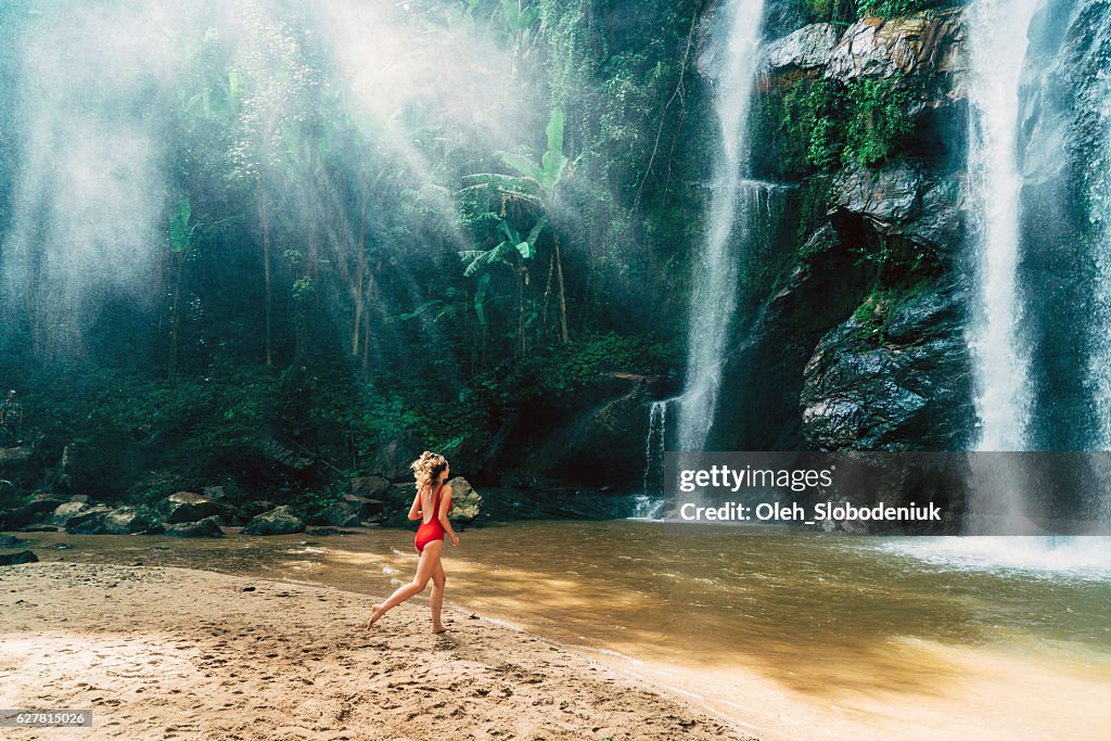 Woman running to tropical waterfall