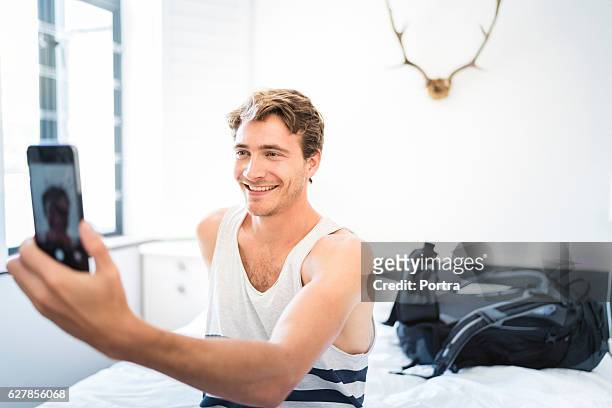 cheerful man taking selfie in hotel room - three quarter length stockfoto's en -beelden