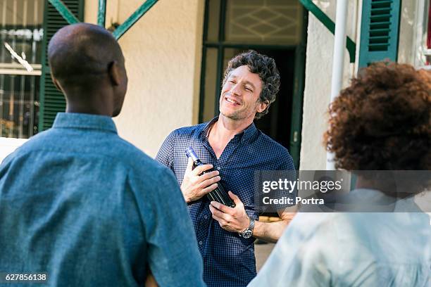 man holding wine bottle while looking at friends - wine gift stock pictures, royalty-free photos & images
