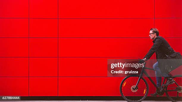 handsome man riding bicycle beside the red wall - when travel was a thing of style stockfoto's en -beelden