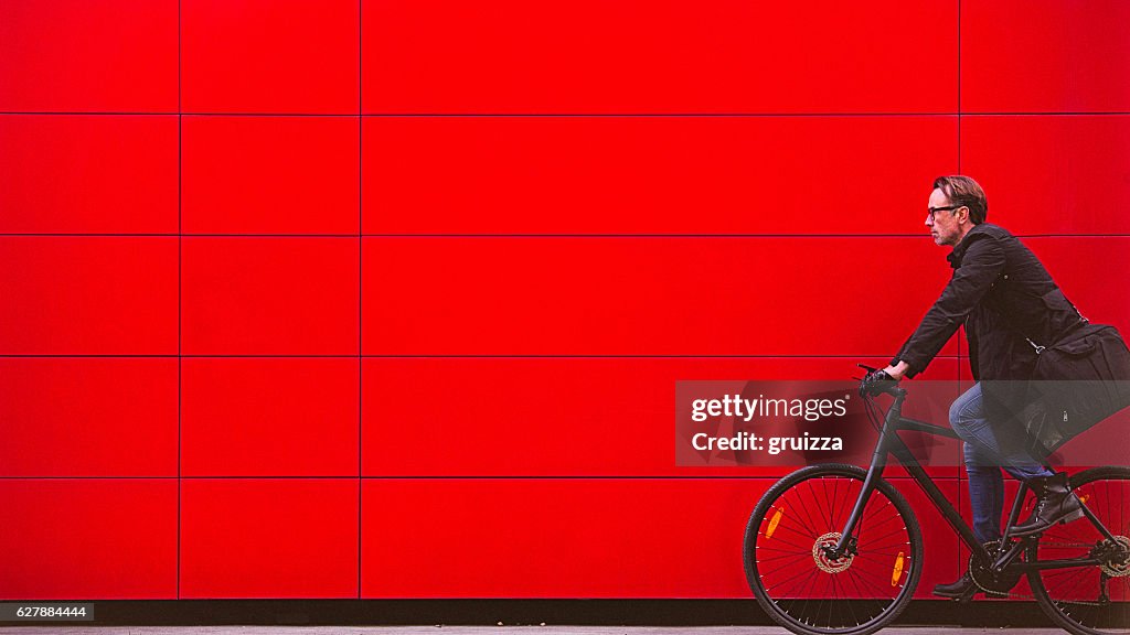 Handsome man riding bicycle beside the red wall