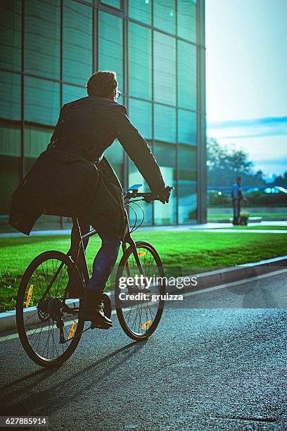 handsome man riding bicycle beside the modern office building - spitsperiode stockfoto's en -beelden