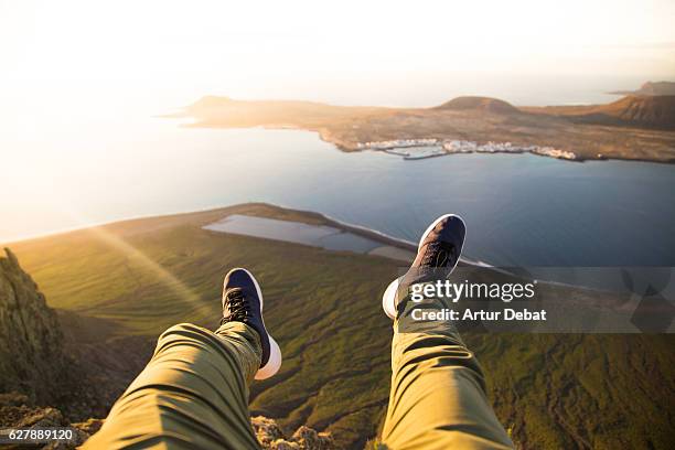 guy from personal perspective flying his legs over the cliff in the volcanic island of lanzarote from nice viewpoint during the sunset light with volcanic islands during a travel vacations through the island. - beautiful legs in high heels stock pictures, royalty-free photos & images