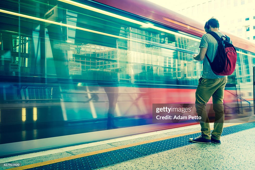 Young man with backpack and headphones waiting for train