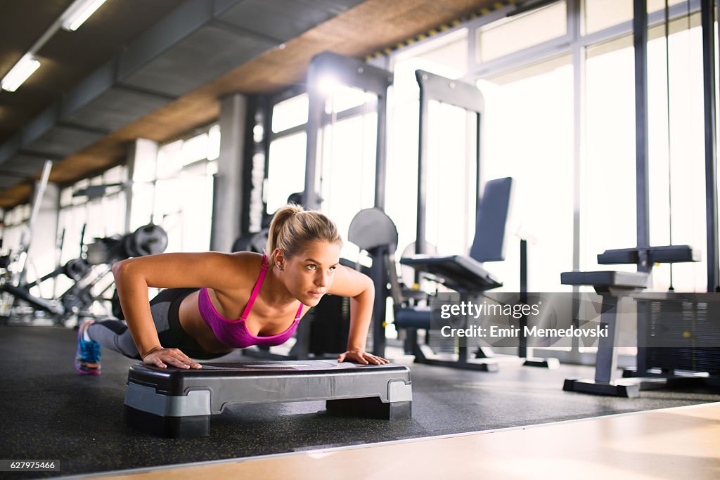Beautiful female doing push-ups on the step aerobics equipment