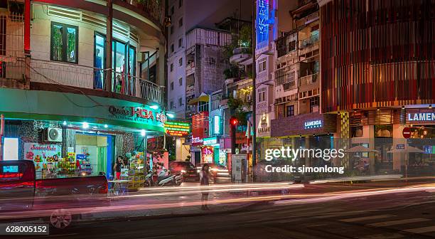 a lady is standing by the road side and ready to cross the road - nightlife stock pictures, royalty-free photos & images