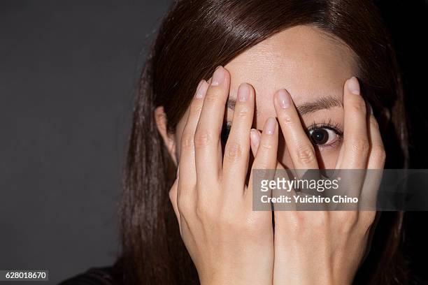 scared woman peeking through her hands - frau erschrocken stock-fotos und bilder