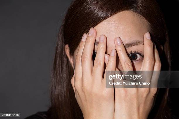 scared woman peeking through her hands - 手を顔にやる ストックフォトと画像