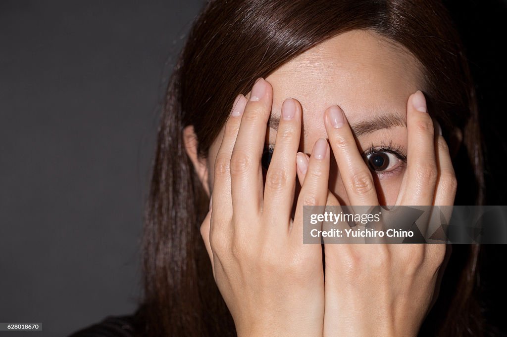 Scared woman peeking through her hands