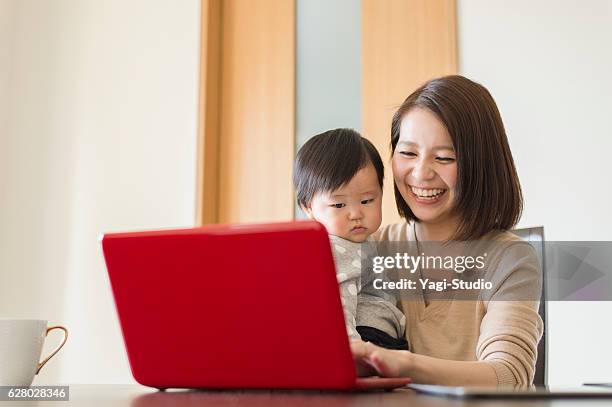 自宅で彼女の女の赤ちゃんと一緒に働く若い母親 - 子供　日本人　笑顔 ストックフォトと画像