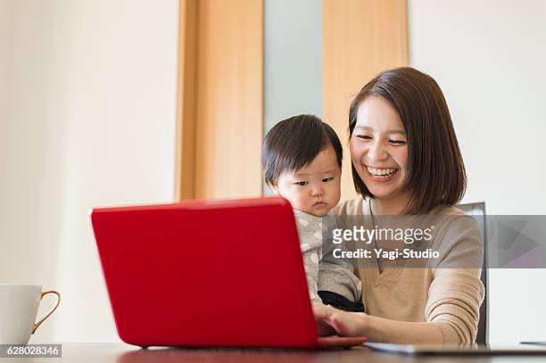 young mother working with her baby girl at home - personal computer 個照片及圖片檔