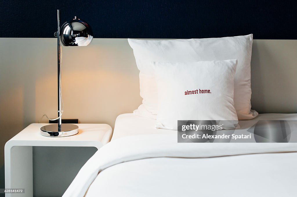 Bed with white linens and a nightstand with lamp in a hotel