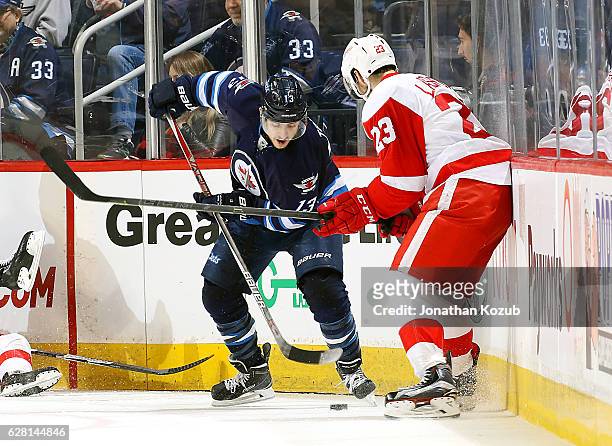 Brandon Tanev of the Winnipeg Jets plays the puck away from Brian Lashoff of the Detroit Red Wings along the corner boards during second period...