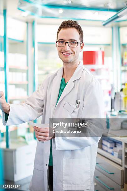 male pharmacist with prescription standing by shelf - cure berlin 2016 stock pictures, royalty-free photos & images