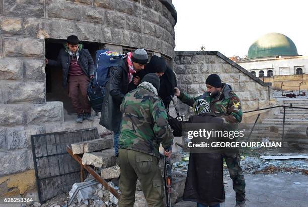 Syrian residents fleeing the violence in the eastern rebel-held parts of Aleppo are helped by pro-government forces as they evacuate from their...