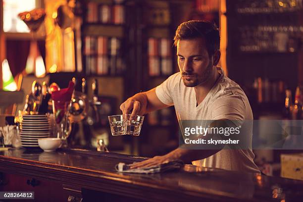 joven camarero masculino limpiando el mostrador de la barra después del trabajo. - barman fotografías e imágenes de stock
