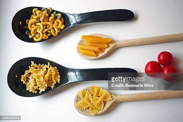 different shapes of italian raw pasta in spoons  cherry tomatoes. - reginette stock pictures, royalty-free photos & images