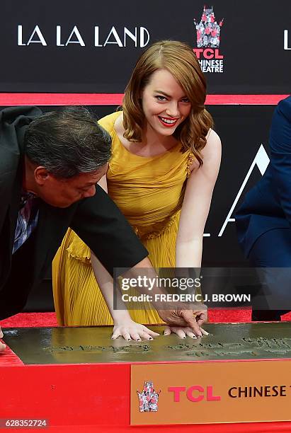 Actress Emma Stone places her hands into the block of cement at the Hand and Foot prints ceremony with actor Ryan Gosling in front of the TCL Chinese...