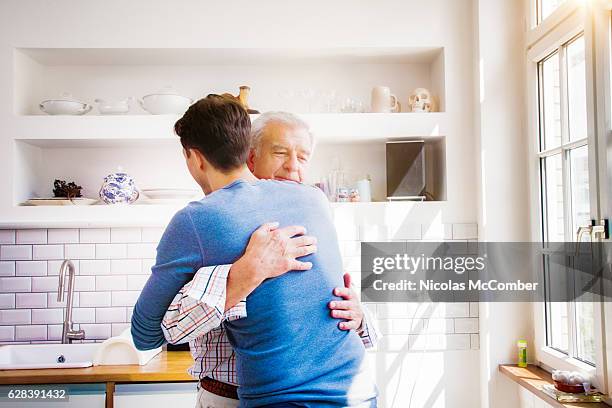 senior mann umarmt reifen sohn in sonniger küche - reconciliation stock-fotos und bilder