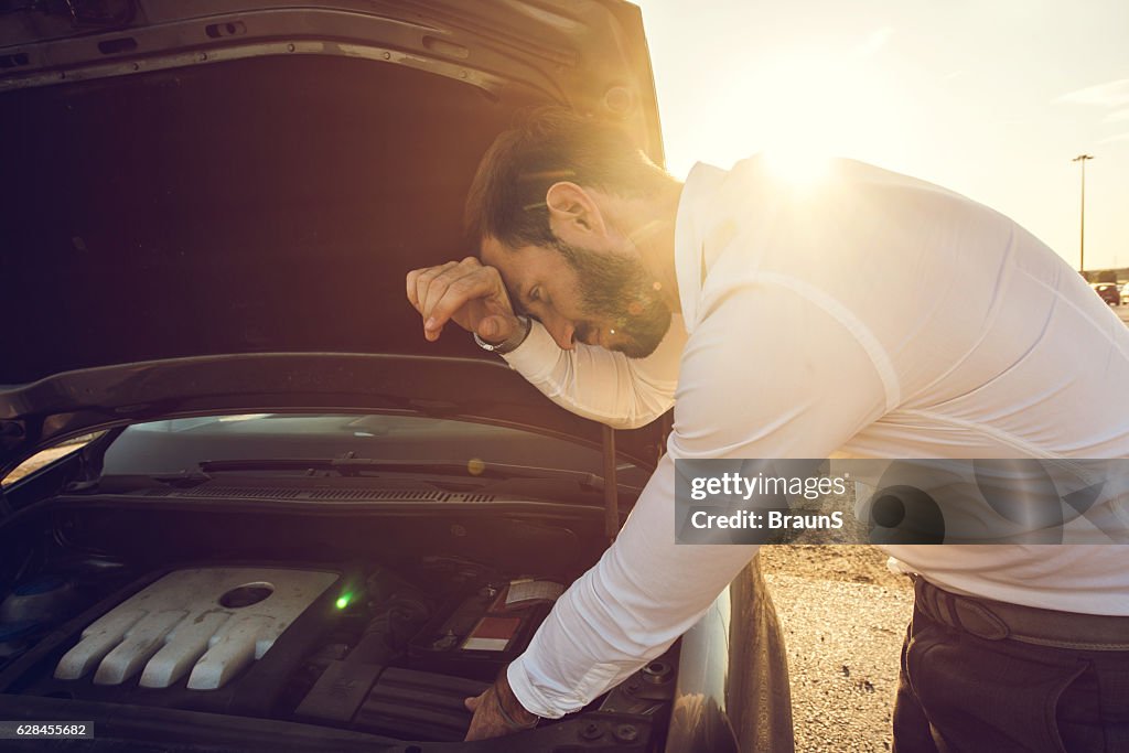 Joven empresario tratando de arreglar su coche al atardecer.