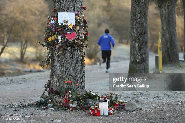 Jogger runs past flowers and messages left by mourners that adorn a tree near the spot where Maria L., a 19-year-old medical student, was raped and...