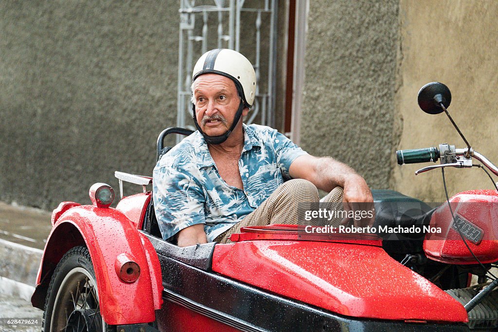 Old man in printed shirt sitting in a rain soaked red side...