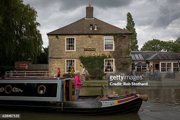 Woman navigates a canal boat down past a pub along the Grand Union Canal on July 10, 2016 in Stoke Bruerne, England. South Northamptonshire is a...