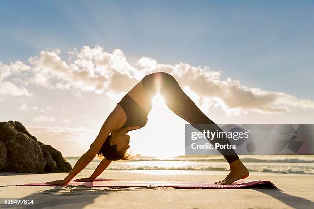 athlet in nach unten gerichteter hundeposition am ufer - woman stretching sunset stock-fotos und bilder