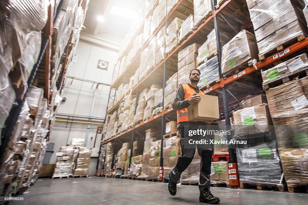 Worker carrying cardboard box in warehouse