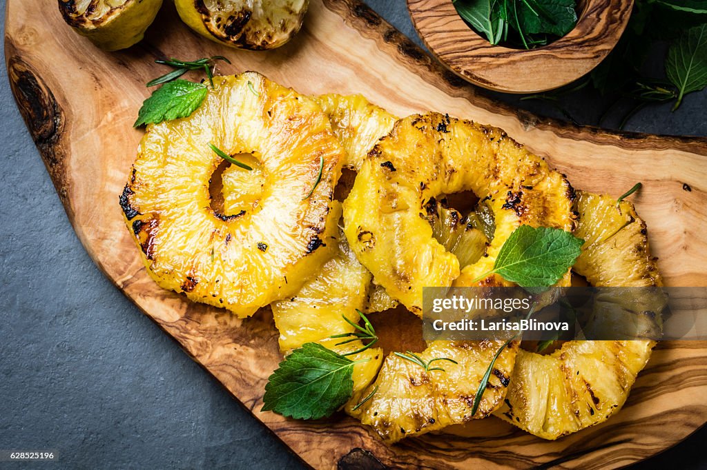 Grilled pineapple slices with fresh mint on olive cutting board